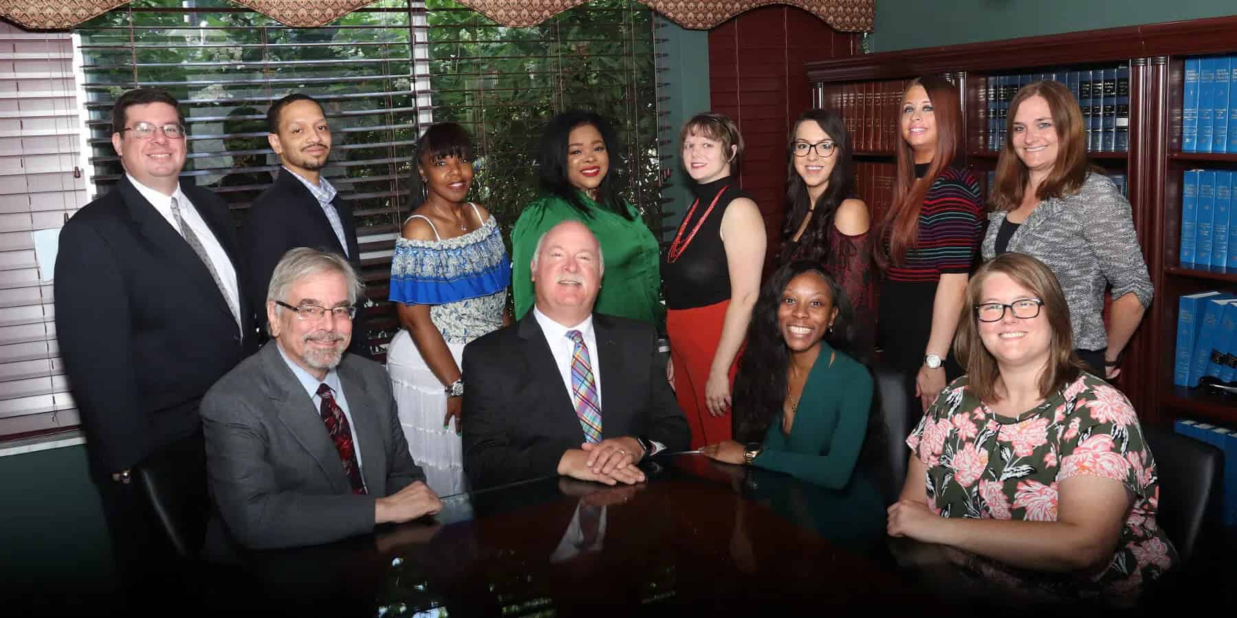 A group of twelve professionally dressed people, including a lawyer, pose together around a table in an office with bookshelves and large windows in the background, suggesting a discussion on finances or credit matters.
